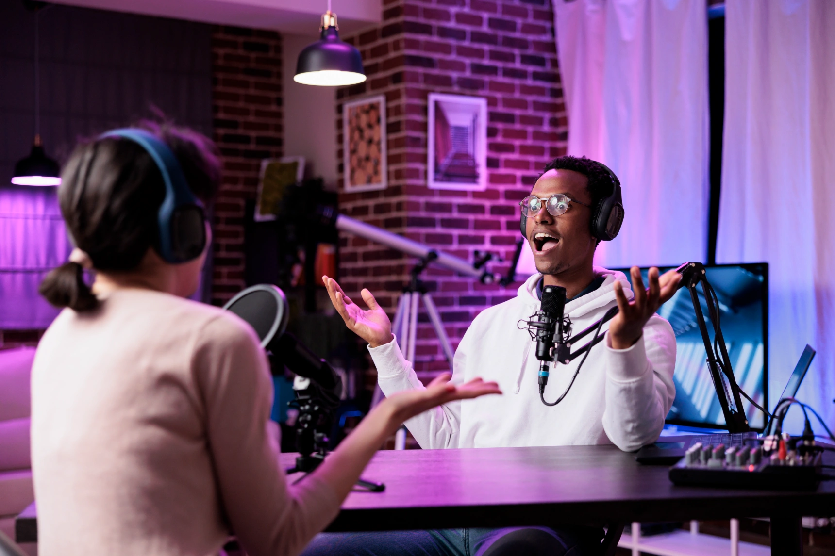 Energetic podcast chat in neon-lit brick studio with laughing male host gesturing.