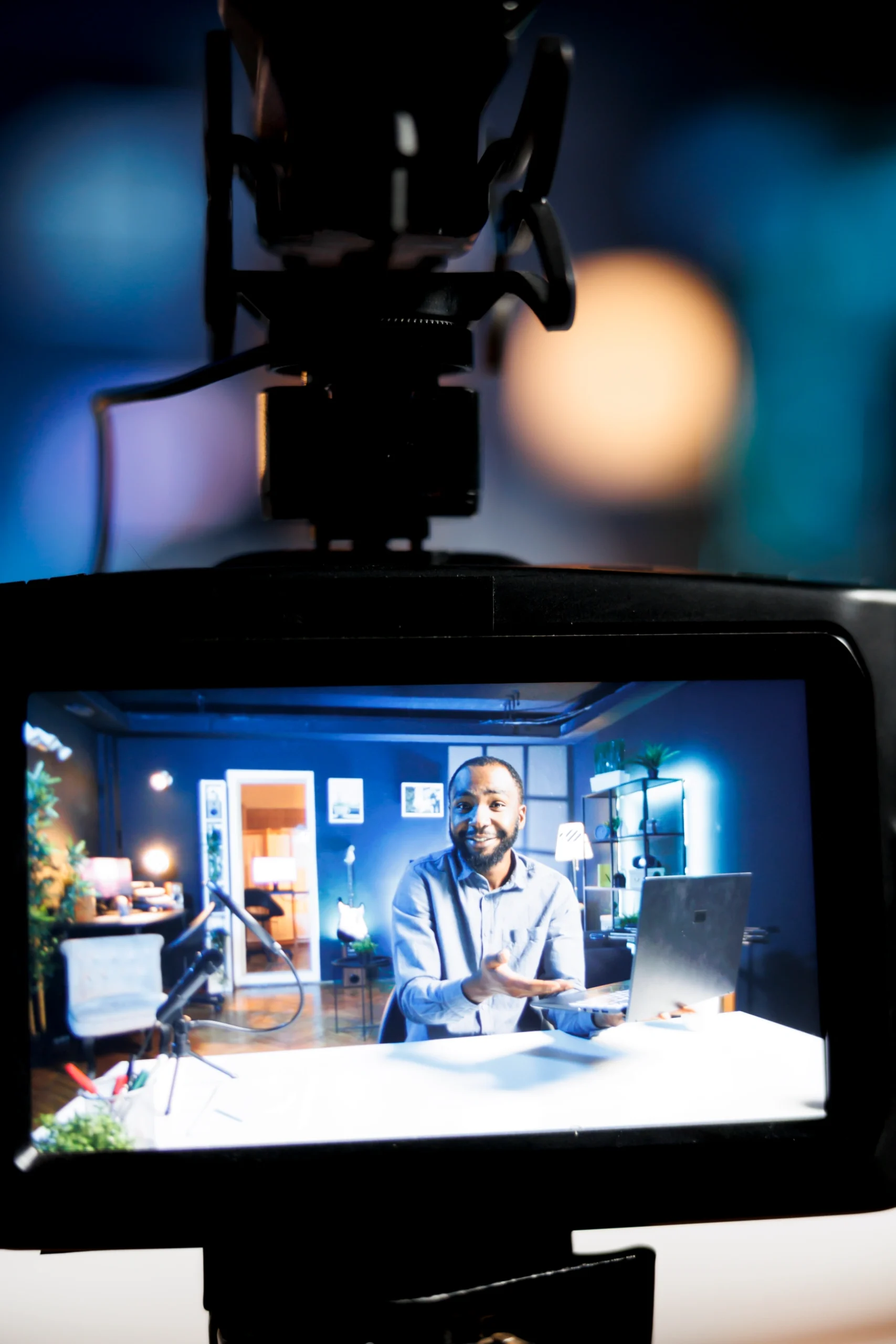 Camera monitor view of a presenter at a desk in a modern studio set-up.