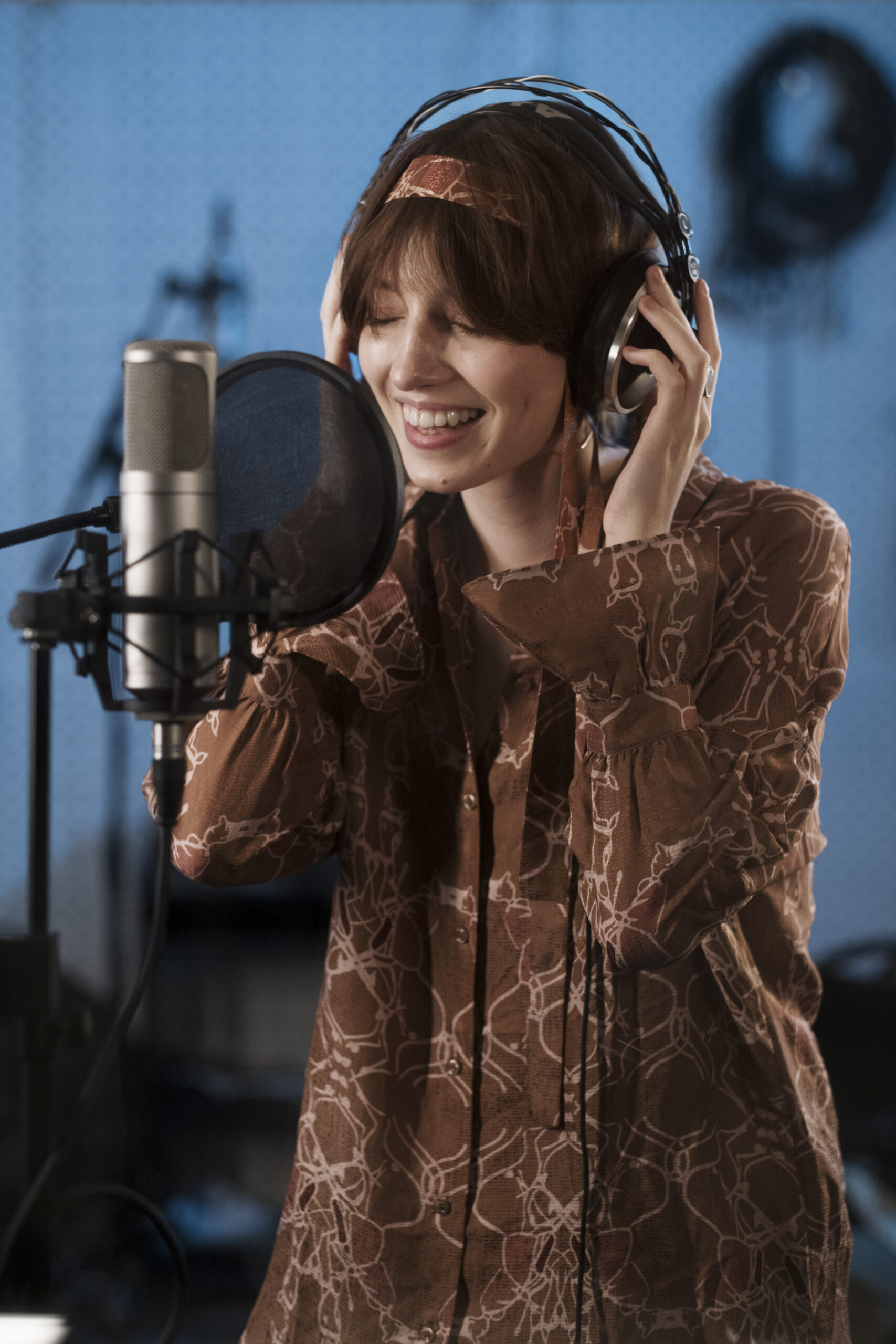 Smiling woman wearing headphones singing into a studio microphone.