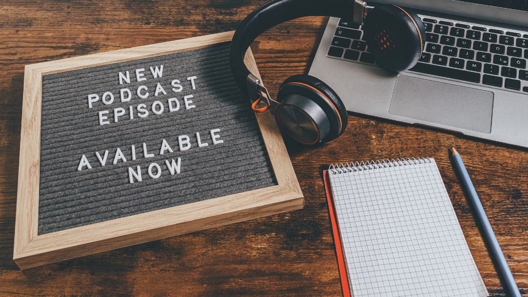 Letter board showing "new podcast episode available now" with headphones, laptop and notepad, answering how often should I release podcast episodes for real growth.