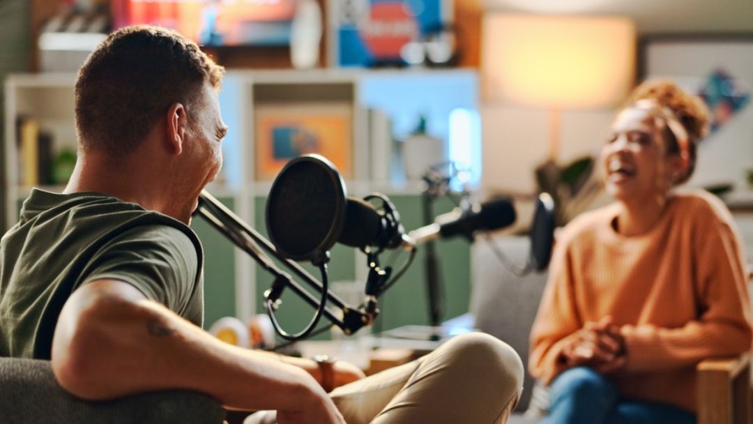 Podcast hosts recording episode together in studio, illustrating pros and cons of outsourcing podcast production versus in-house production management